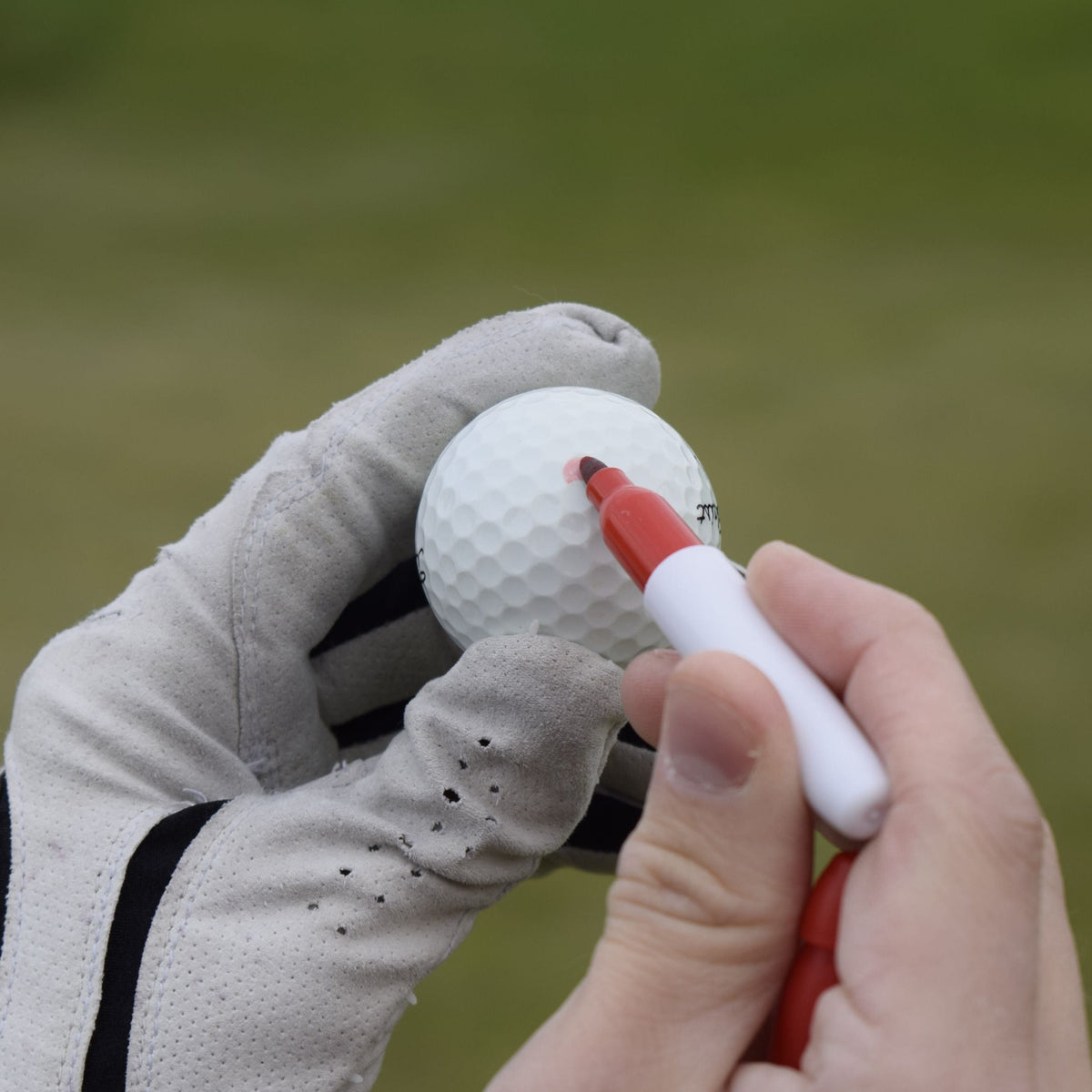 En närbild när en person med golfhandske använder marker pen för att markera på sin golfboll.