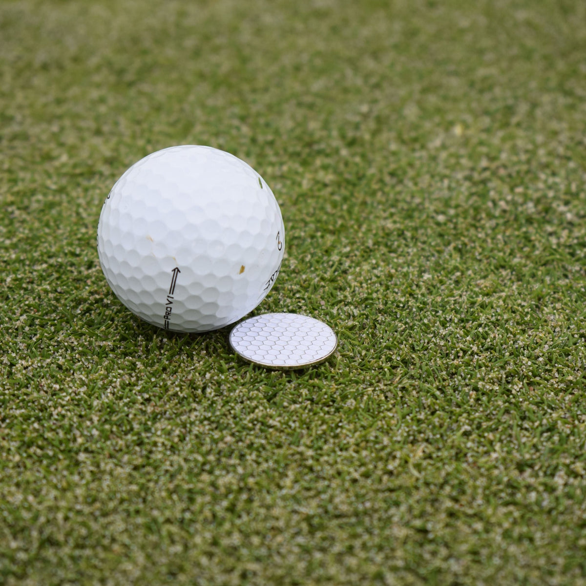 Närbild på markören som fäljer med när du köper Pitchfork marker som ligger på en golf green bakom en golfboll. 