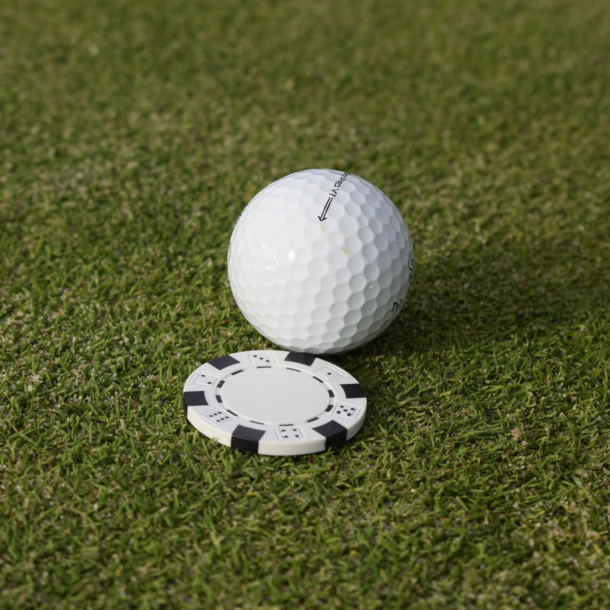 Närbild på den vita markören som följer med när du köper Poker ballmarker som ligger på en greenn bakom en golfboll.