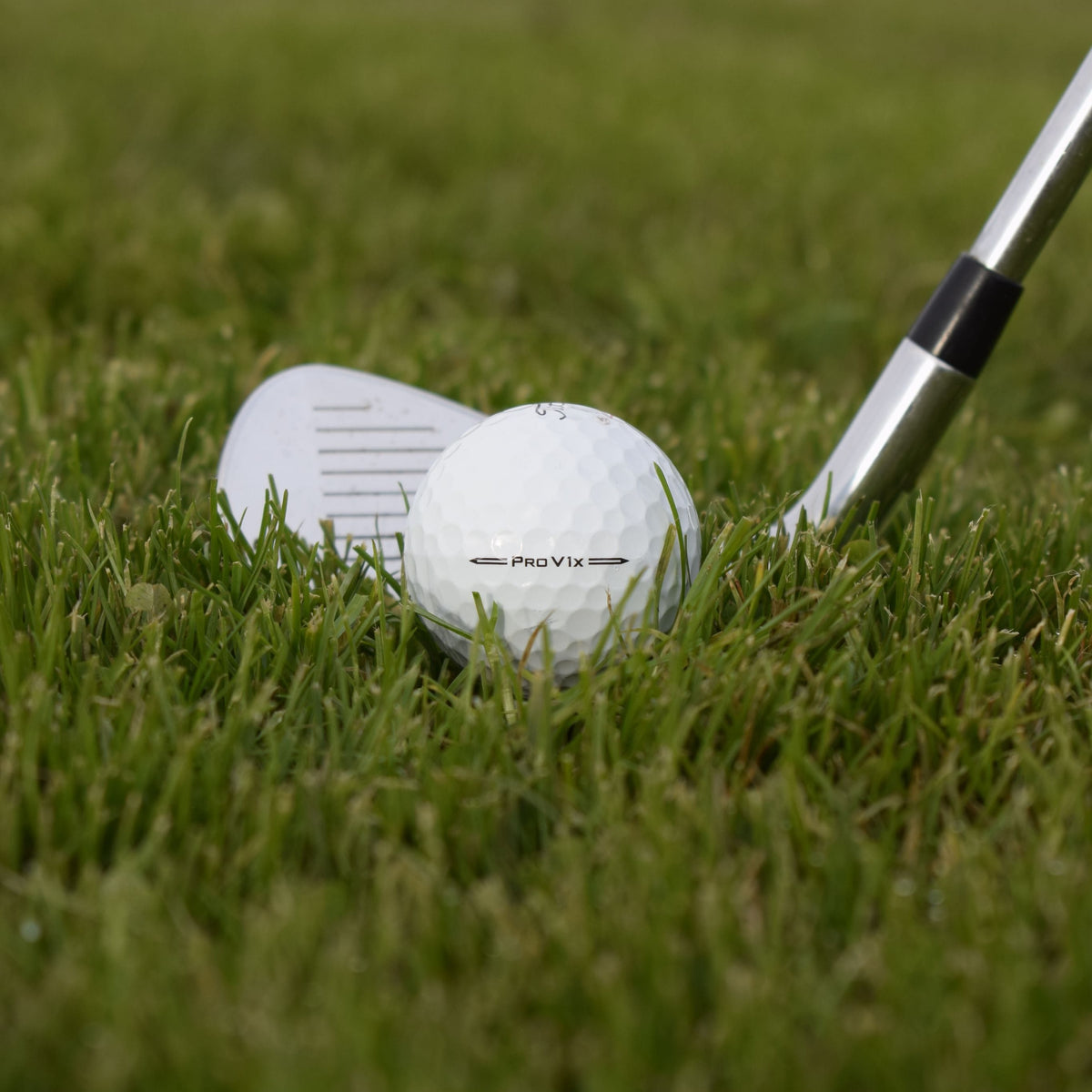 Närbild på en Titleist Pro V1x golfboll som ligger i gräset framför en golfklubba.
