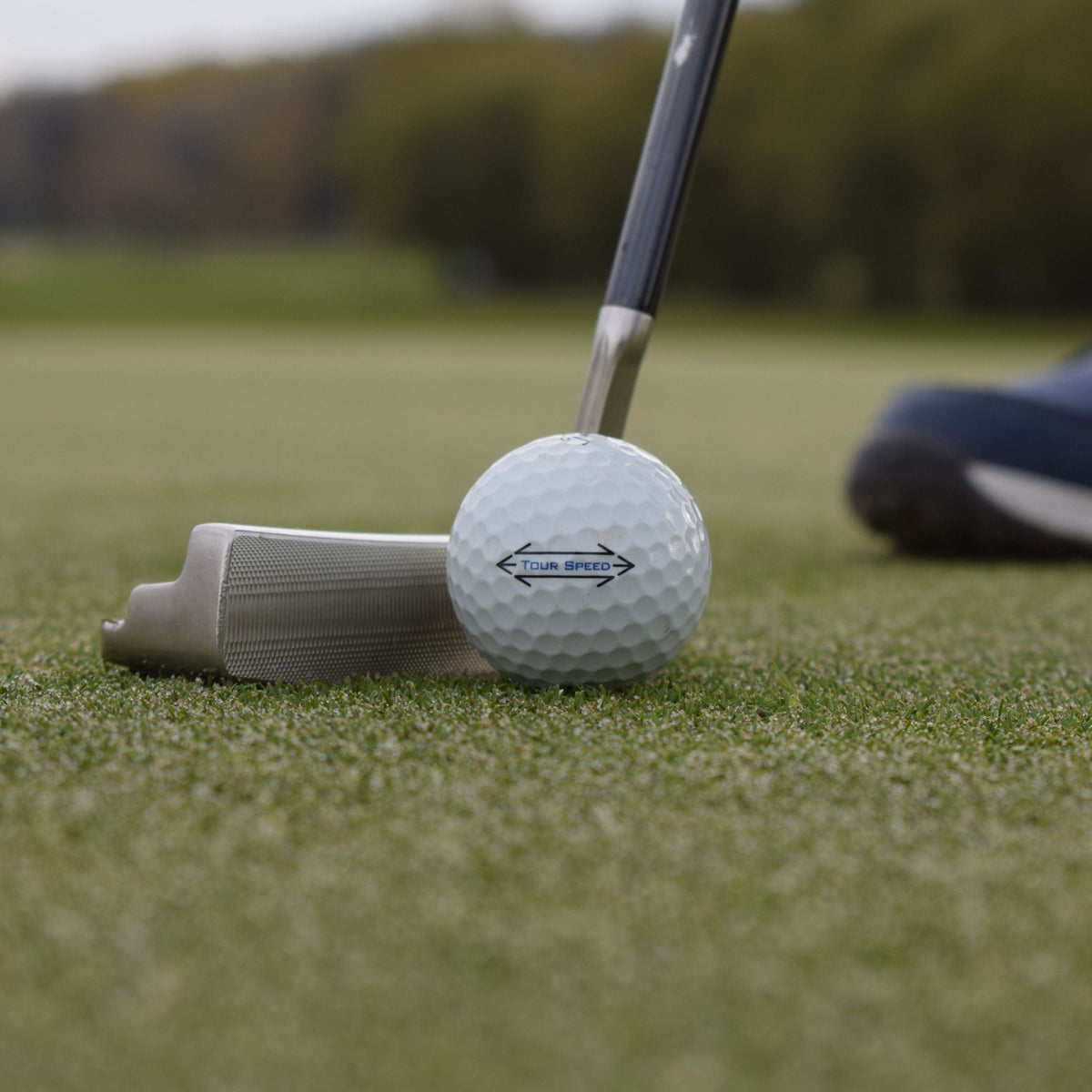 En närbild på en titleist tour speed golfboll på en golf green framför en putter.