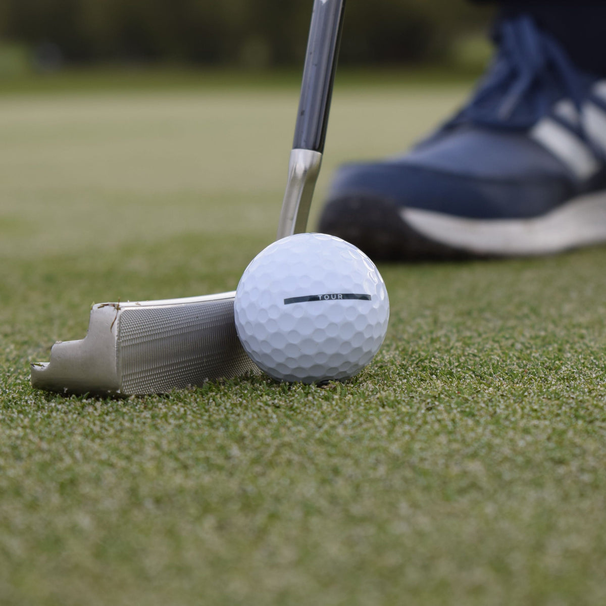 En närbild på en Vice Tour Golfboll som ligger på en green och framför en putter.