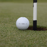 En Närbild på Wilson Staff Triad golfboll som ligger precis vid hålet på en golfbana.
